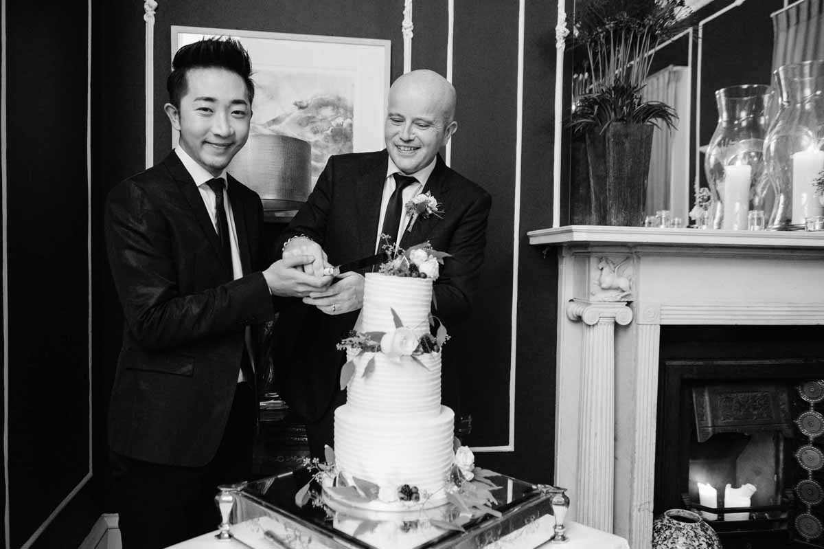 LGBTQ wedding photography of two grooms cutting their wedding cake during their wedding reception at No. 25 Fitzwilliam Place in Dublin