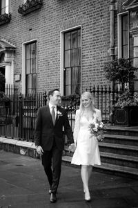 The bride and groom walk hand in hand along Merrion Row in Dublin during their Merrion Hotel wedding